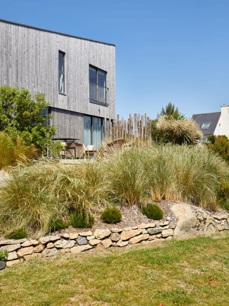 massif de graminées devant maison moderne avec muret en pierre naturelle